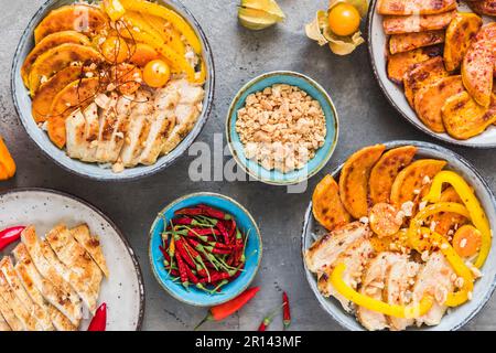 Zwei buddha-Schüsseln mit scharfem Huhn, Reis, Paprika, Süßkartoffel und gehackten Erdnüssen, Trend und gesundem Essen, Draufsicht auf grauem Hintergrund Stockfoto