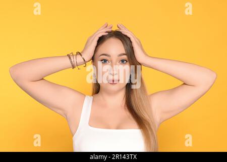 Junge Frau mit Lippen- und Ohrmuscheln auf gelbem Hintergrund Stockfoto