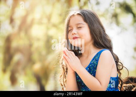 Wunderschönes glückliches Mädchen, das im Park mit blauem Kleid ohne Schuhe spielt, auf dem Baum sitzt und vor Glück schreit, während die Familie Kinder genießt Stockfoto