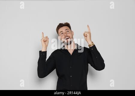 Ein gutaussehender Mann in schwarzem Hemd, der auf etwas auf hellgrauem Hintergrund zeigt Stockfoto