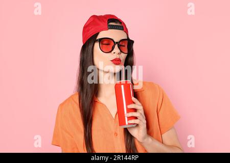 Schöne junge Frau, die aus der Blechdose trinkt, auf pinkfarbenem Hintergrund Stockfoto