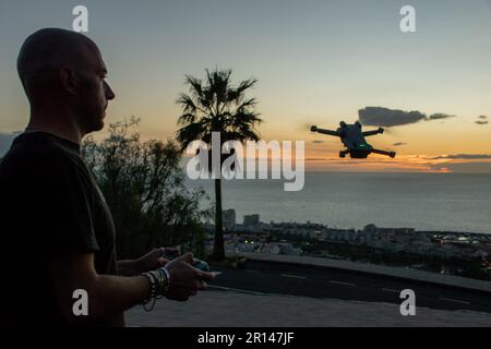 Ein weißer Mann kontrolliert seine Drohne bei Sonnenuntergang an einem tropischen Ort. Unbemannte Flugzeuge Stockfoto