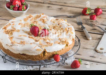 Ganze Rhabarberkuchen mit Baiser-Belag, geröstete Mandeln und frische Erdbeeren auf einem Kühlregal auf einem alten rustikalen Holztisch Stockfoto