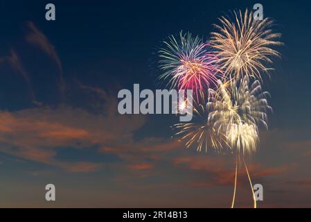 Helles und farbenfrohes Feuerwerk, das in einem dunkelblauen Himmel mit Wolken explodiert. Hintergrund für Geburtstagsfeiern, große Veranstaltungen und Partys wie den 4. Juli Stockfoto