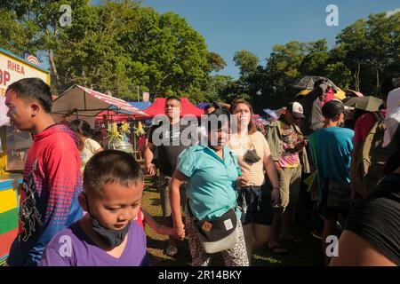 Malaybalay, Philippinen - eine Frau hält die Hand des Kindes fest, während sie beim Kaamulan Festival zwischen Menschenmassen und farbenfrohen Imbissständen spaziert. Stockfoto