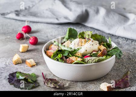 Gemischter Salat mit Radieschen, hausgemachten Croutons und Burrata-Käse auf grauem Hintergrund Stockfoto