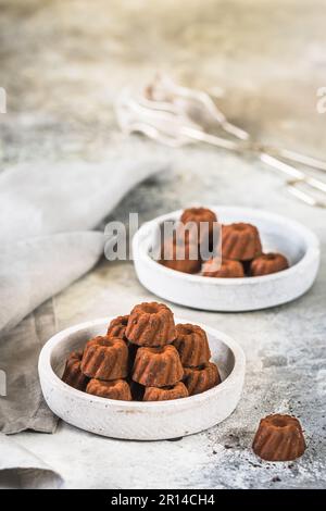 Pralinen aus Schokolade in Form von kleinen Guglhupf-Törtchen, kakaogetränkt, auf hellgrauem Hintergrund, vertikal mit Kopierbereich Stockfoto