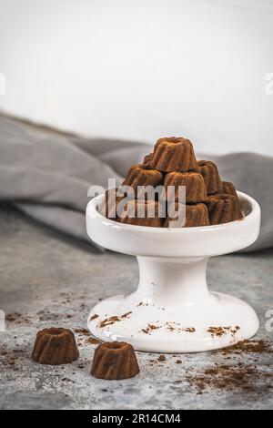Pralinen aus Schokolade in Form von kleinen Bundt-Kuchen, mit Kakao bestaubt, auf hellgrauem Hintergrund, Kopierraum Stockfoto