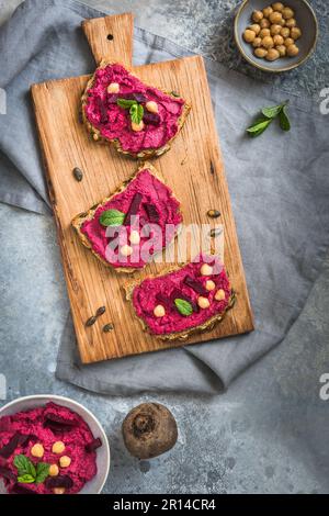 Holzbrett mit Brotscheiben mit Rote-Bete-Hummus auf grauem Hintergrund, Draufsicht Stockfoto