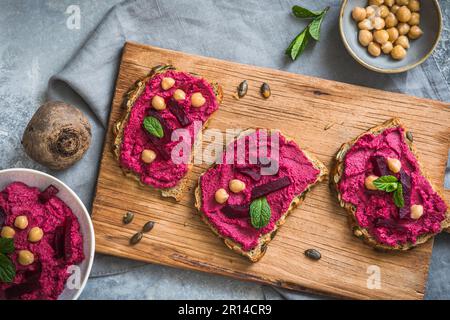 Holzbrett mit Brotscheiben mit Rote-Bete-Hummus auf grauem Hintergrund, Draufsicht Stockfoto