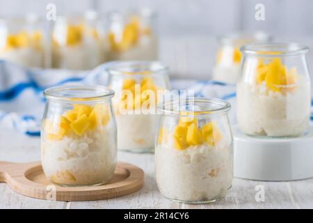Kokosreis-Pudding mit Mango in Dessertgläsern auf weißem Holzhintergrund Stockfoto