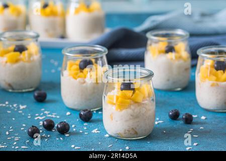 Kokosreis-Pudding mit Mango in Dessertgläsern auf blauem Hintergrund Stockfoto