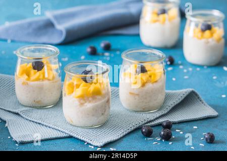 Kokosreis-Pudding mit Mango in Dessertgläsern auf blauem Hintergrund Stockfoto