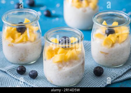 Kokosreis-Pudding mit Mango in Dessertgläsern auf blauem Hintergrund Stockfoto