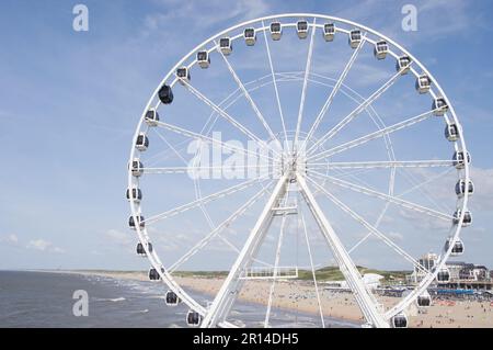 Den Haag, Niederlande - 24. August 2021: Riesenrad des Piers in Scheveningen mit einem überfüllten Strand im Hintergrund Stockfoto