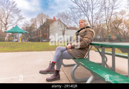 Eine ältere Frau sitzt allein auf einer Parkbank Stockfoto