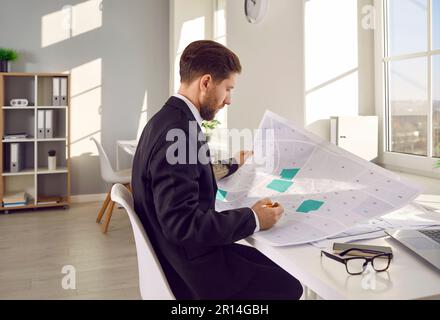 Professioneller Kartograf, der an seinem Arbeitsplatz mit einer gedruckten Katasterkarte arbeitet. Stockfoto