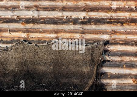 Alte Fischernetze trocknen an einem sonnigen Wintertag an der Holzwand eines Holzhauses. Stockfoto