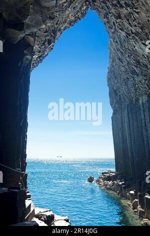 Die Insel Iona kann vom Inneren der berühmten Fingal's Cave auf der Insel Staffa aus gesehen werden, dunkle Basaltsäulen vor blauem Sommerhimmel, innere Hebriden, Schottland. Stockfoto