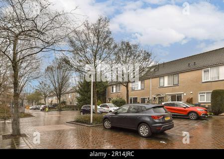 Eine Straße mit Autos, die an der Seite geparkt sind, und Häuser im Hintergrund, alle mit Sonnenschirmen bedeckt Stockfoto
