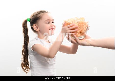 Das kleine Mädchen bekommt eine große Schüssel Chips, Snacks mit Schmalz, weißes Hintergrundporträt, wie ein kleines Mädchen Chips isst. Stockfoto