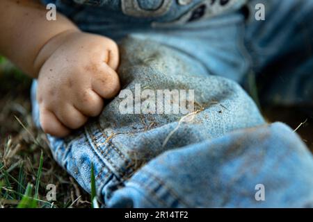 Ein Baby, das schmutzige Jeans trägt, nachdem es im Dreck gespielt hat, ohne Gesicht Stockfoto