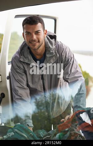 Alles zusammengepackt und fertig. Porträt eines gutaussehenden jungen Mannes, der Ausrüstung aus einem Auto holt. Stockfoto