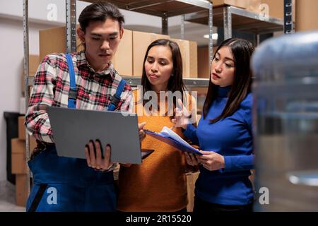 Lagermitarbeiter, die den Empfang und Versand von Paketen online auf einem Laptop verwalten. Das Team der Lagermanager bespricht Inventarberichte und arbeitet im Lagerraum zusammen Stockfoto