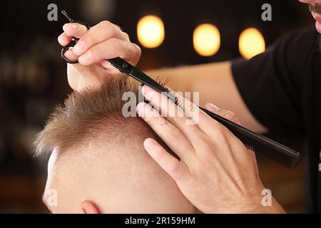 Nahaufnahme eines unbekannten Friseurlehrers von Herrenfrisuren ergibt einen neuen, stilvollen Haarschnitt mit einer speziellen professionellen Schere und einem Kamm für einen Kunden in Stockfoto