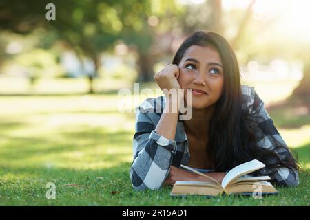 Entspannen mit einem guten Buch. Eine junge Frau liegt auf Gras und liest ein Buch. Stockfoto