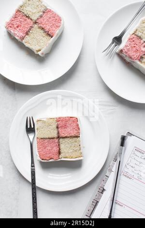 Draufsicht auf battenburger Kuchenstück auf weißem Teller, Mandel- und Erdbeerschwammkuchen bedeckt mit weißem Fondant, Querschnitt aus rosa und gelbem Karo Stockfoto