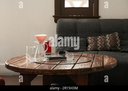 Manuelle Kaffeemühle mit Bohnen, Glaskanne und Wellentrockner auf Holztisch im Café Stockfoto