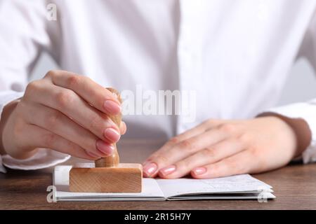 Ukraine, Lemberg - 6. September 2022: Frau stempelt Visumseite im Reisepass am Holztisch ab, Nahaufnahme Stockfoto