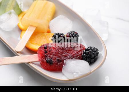 Teller mit köstlichem Eis am Stiel, Eiswürfeln und frischem Obst auf einem weißen Tisch Stockfoto