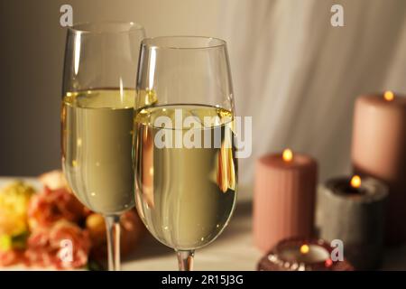 Gläser Sekt, Blumen und brennende Kerzen auf weißem Tisch, Nahaufnahme Stockfoto