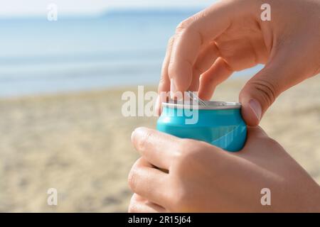 Frau öffnet Aluminiumdose mit Getränk am Strand, Nahaufnahme. Platz für Text Stockfoto