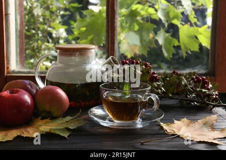 Heißer Tee, Äpfel und trockene Blätter auf Holzfenstern. Herbstatmosphäre Stockfoto