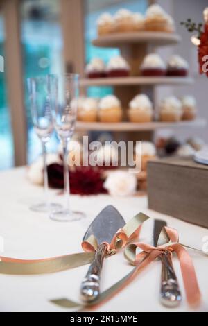 Hochzeitstorte mit Utensilien, im Hintergrund unscharf, roter Samt und Vanille. Champagnerflöten, Hochzeitsempfang Stockfoto