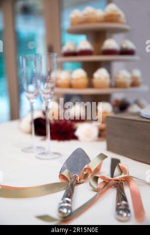 Hochzeitstorte mit Utensilien, im Hintergrund unscharf, roter Samt und Vanille. Champagnerflöten, Hochzeitsempfang Stockfoto