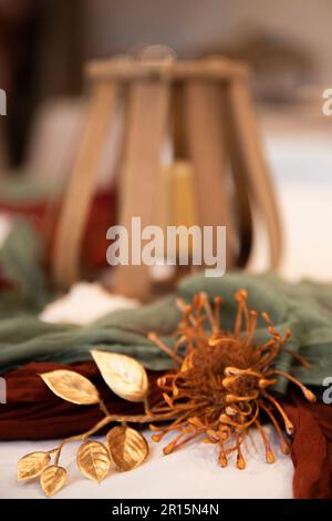 Nahaufnahme der Hochzeitsdekoration mit Holzlaternen, mit Schwerpunkt auf dekorativen Stoffen und Seidenblumen, künstlichen Blumen, verschwommenem Hintergrund Stockfoto
