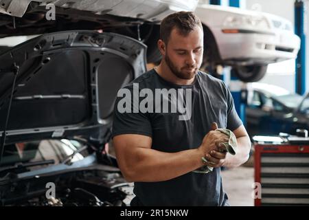 Ich mache mir die Hände schmutzig, um sicherzustellen, dass Ihr Auto optimal funktioniert. Ein Mechaniker, der mit einem Tuch seine schmutzigen Hände abwischte. Stockfoto