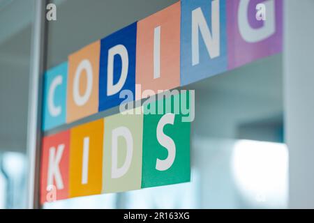 Klassenzimmer in einer Schule programmieren. Türschild mit farbigen Buchstaben, auf denen „Kinder kodieren“ steht, auf einem Klasseneingang in einer Grundschule. Stockfoto