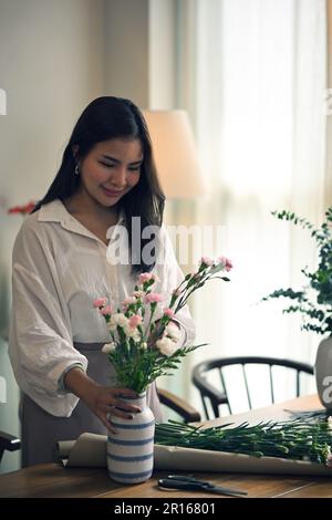 Das Porträt einer wunderschönen jungen Asiatin mag es, eine Vase mit wunderschönen Blumen zu Hause zu arrangieren. Freizeitkonzept Stockfoto