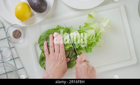 Eine Frau, die Romaine Salat aus Sellerie macht. Blätter von frischem grünen Salat Nahaufnahme auf einem weißen Schneidebrett, Blick von oben Stockfoto