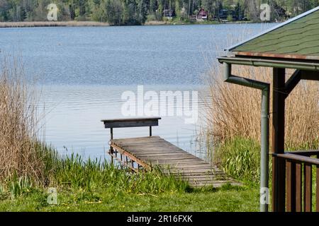 Ein einfacher hölzerner Pier am Ufer eines Sees oder Teiches in Holany, Tschechische Republik. Gras und Wald und Ferienhäuser. Ruhige Urlaubsatmosphäre. Stockfoto