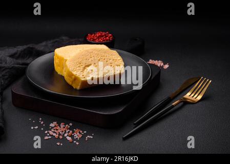 Köstliches Omelett mit Milch, Gewürzen und Kräutern, die auf einer Keramikplatte auf dunklem Betonhintergrund in große Stücke geschnitten wurden Stockfoto