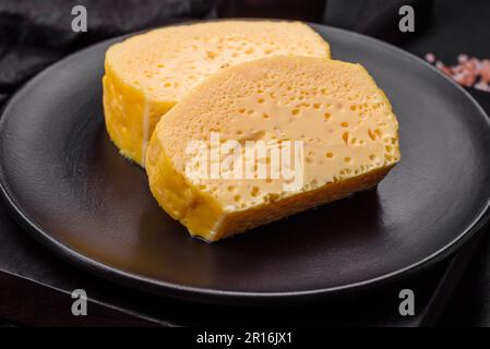 Köstliches Omelett mit Milch, Gewürzen und Kräutern, die auf einer Keramikplatte auf dunklem Betonhintergrund in große Stücke geschnitten wurden Stockfoto