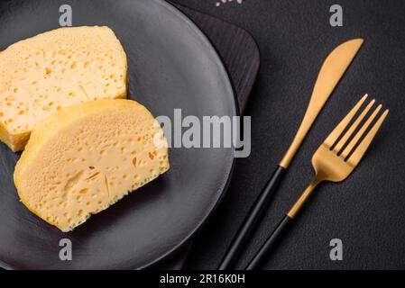 Köstliches Omelett mit Milch, Gewürzen und Kräutern, die auf einer Keramikplatte auf dunklem Betonhintergrund in große Stücke geschnitten wurden Stockfoto