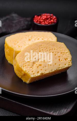 Köstliches Omelett mit Milch, Gewürzen und Kräutern, die auf einer Keramikplatte auf dunklem Betonhintergrund in große Stücke geschnitten wurden Stockfoto