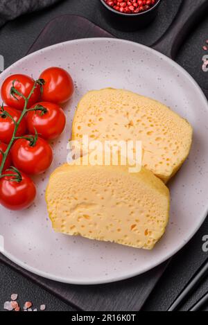 Köstliches Omelett mit Milch, Gewürzen und Kräutern, die auf einer Keramikplatte auf dunklem Betonhintergrund in große Stücke geschnitten wurden Stockfoto